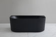 Black freestanding bathtub on a light gray floor with a neutral gray wall background